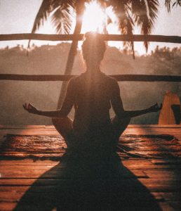 Woman meditating on a deck outside with a  palm tree in the background